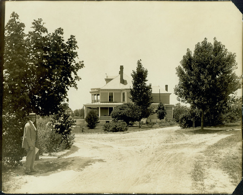 Kilgo in front of his home. There is a dirt road and a good deal of bushes and small trees around the property.